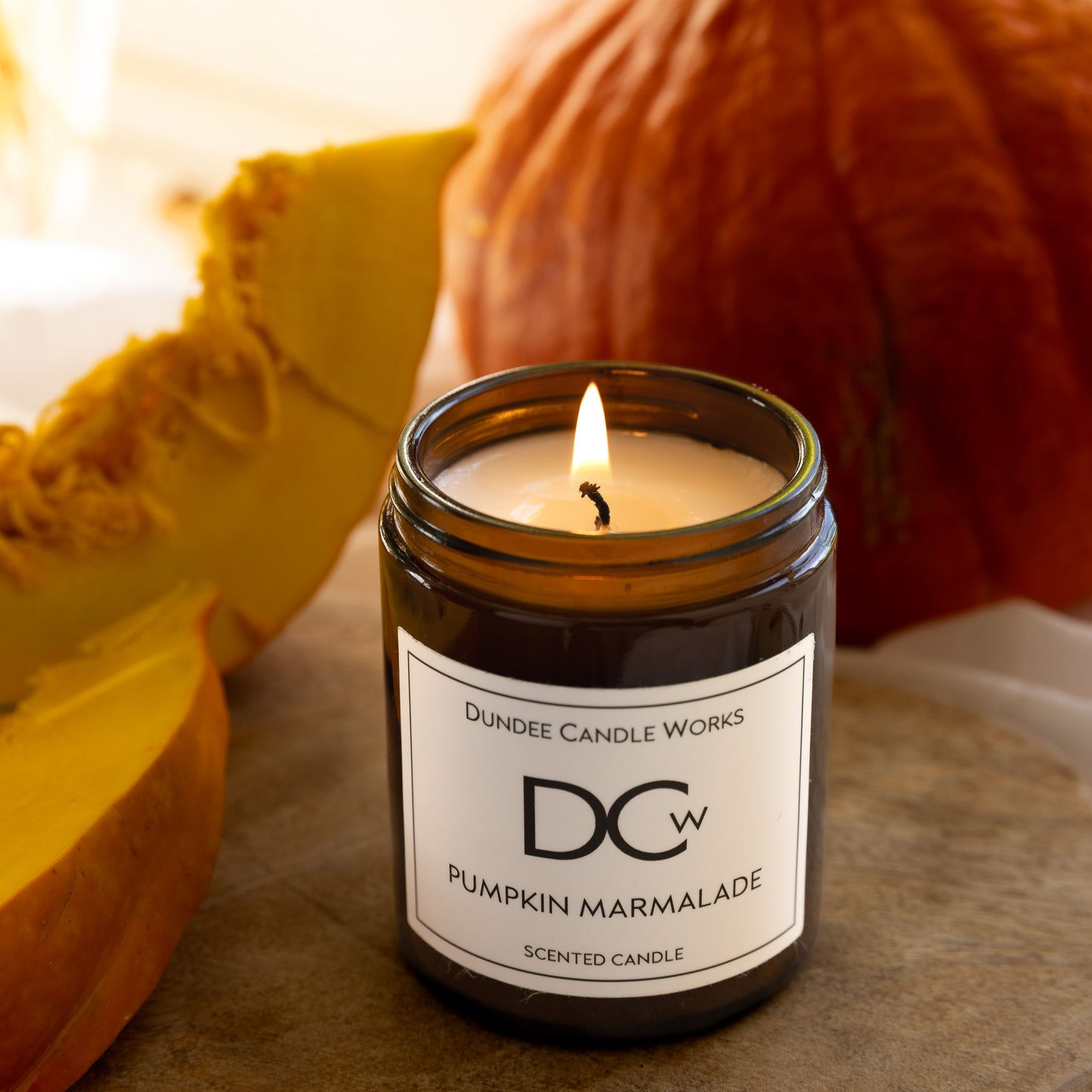 Candle in a jar labeled 'Dundee Candle Works Pumpkin Marmalade' with pumpkins in the background.