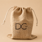 A large natural jute drawstring pouch with white cords and a black embroidered monogram logo reading 'DCW' on the front, set against a solid beige background.