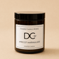 An amber glass jar candle with a black lid and a white label reading 'Dundee Candle Works DCw Apricot Marmalade Scented Candle' on a warm beige background.