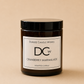 A dark amber glass jar candle with a black lid and a white label reading 'Dundee Candle Works DCW Cranberry Marmalade Scented Candle' on a warm beige background.