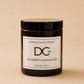 A dark amber glass jar candle with a black lid and a white label reading 'Dundee Candle Works DCW Cranberry Marmalade Scented Candle' on a warm beige background.
