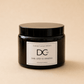 A dark amber glass jar candle with a black lid and a white label reading 'Dundee Candle Works DCw Earl Grey & Verbena Scented Candle' on a warm beige background.