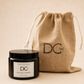 A black glass jar candle with a black lid and a white label reading 'Dundee Candle Works DCw Earl Grey & Verbena Scented Candle' sits in front of a natural jute drawstring pouch printed with 'DCw' on a warm beige background.