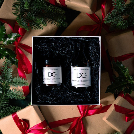 A Cranberry Marmalade candle and Marmalade Gingerbread Diffuser in a white gift box surrounded by Christmas wrapping paper and holly leaves.