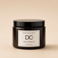 A dark amber glass jar candle with a black lid and a white label reading 'Dundee Candle Works DCw Firs & Fairways Scented Candle' on a warm beige background.