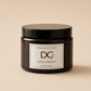 A dark amber glass jar candle with a black lid and a white label reading 'Dundee Candle Works DCw JUTE & TOBACCO SCENTED CANDLE' on a warm beige background.