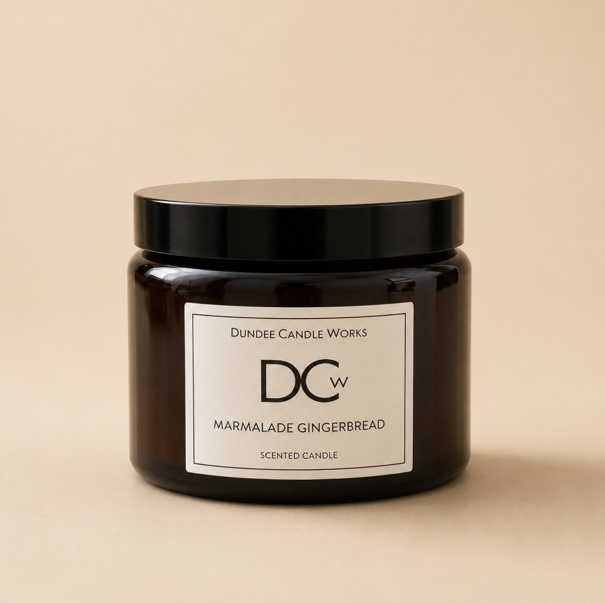 A dark amber glass jar candle with a black lid and a white label reading 'Dundee Candle Works Marmalade Gingerbread' on a warm beige background.