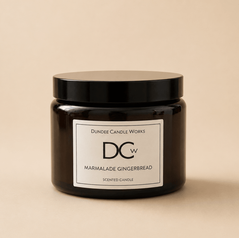 A dark amber glass jar candle with a black lid and a white label reading 'Dundee Candle Works Marmalade Gingerbread' on a warm beige background.