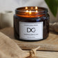 A lit amber glass jar candle from Dundee Candle Works, labeled 'Marmalade & Lime', resting on a wooden surface with a jute bag nearby.