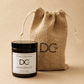 A scented candle jar with a black lid and white label in front of a natural jute drawstring pouch. The label reads 'Dundee Candle Works' and 'Marmalade & Lime', and the candle and pouch both have a 'DCw' logo.