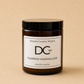 An amber glass jar candle with a black lid and a white label reading 'Dundee Candle Works DCw Pumpkin Marmalade Scented Candle' on a warm beige background.