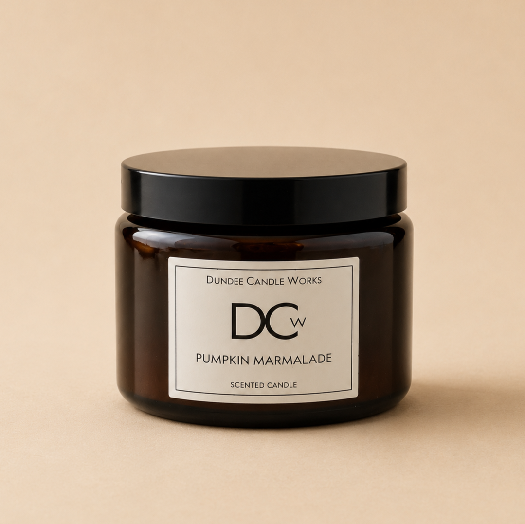 A dark amber glass jar candle with a black lid and a white label reading 'Dundee Candle Works DCw Pumpkin Marmalade Scented Candle' on a warm beige background.