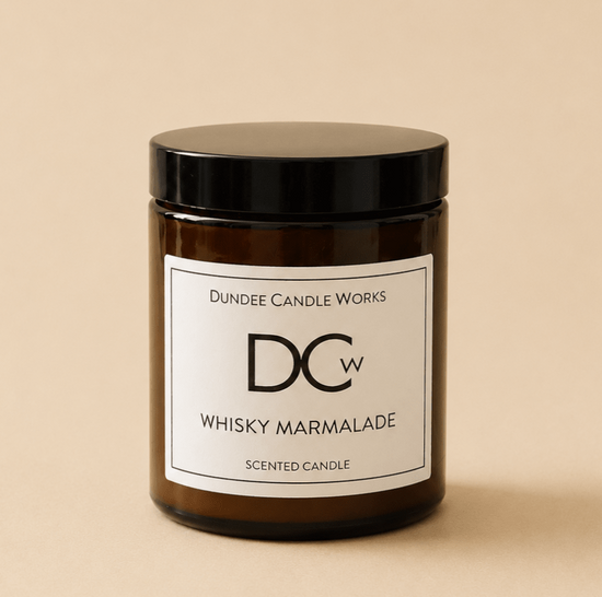 A single amber glass candle jar with a black lid and a white label reading 'Dundee Candle Works DCw Whisky Marmalade Scented Candle' on a warm beige background.