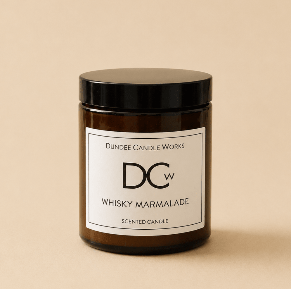 A single amber glass candle jar with a black lid and a white label reading 'Dundee Candle Works DCw Whisky Marmalade Scented Candle' on a warm beige background.