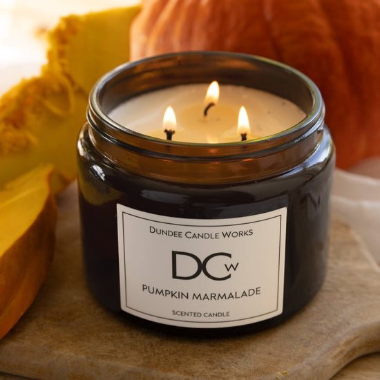 Scented candle in a jar labeled 'Pumpkin Marmalade' from Dundee Candle Works, surrounded by pumpkins.