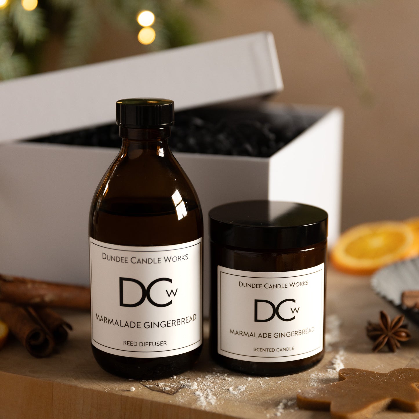 Dundee Candle Works Marmalade Gingerbread candle and diffuser in front of white gift box on a wooden surface with decorative elements.