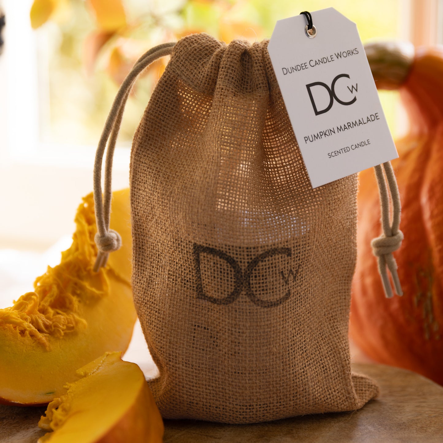 Jute bag with a pumpkin marmalade scented candle and a visible brand tag with pumpkins in background.