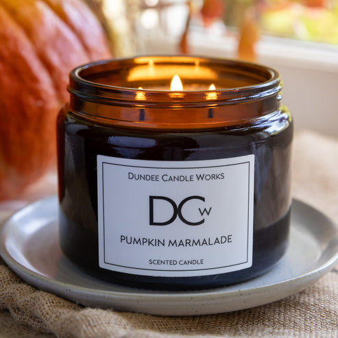 Triple wick amber Pumpkin Marmalade candle with a white label reading 'Dundee Candle Works Pumpkin Marmalade' on a white plate.